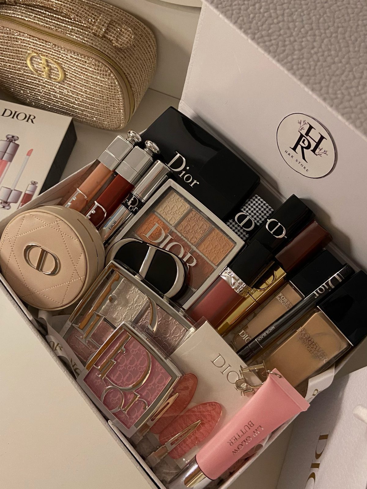 Dior beauty products and a gold handbag arranged in a white gift box.
