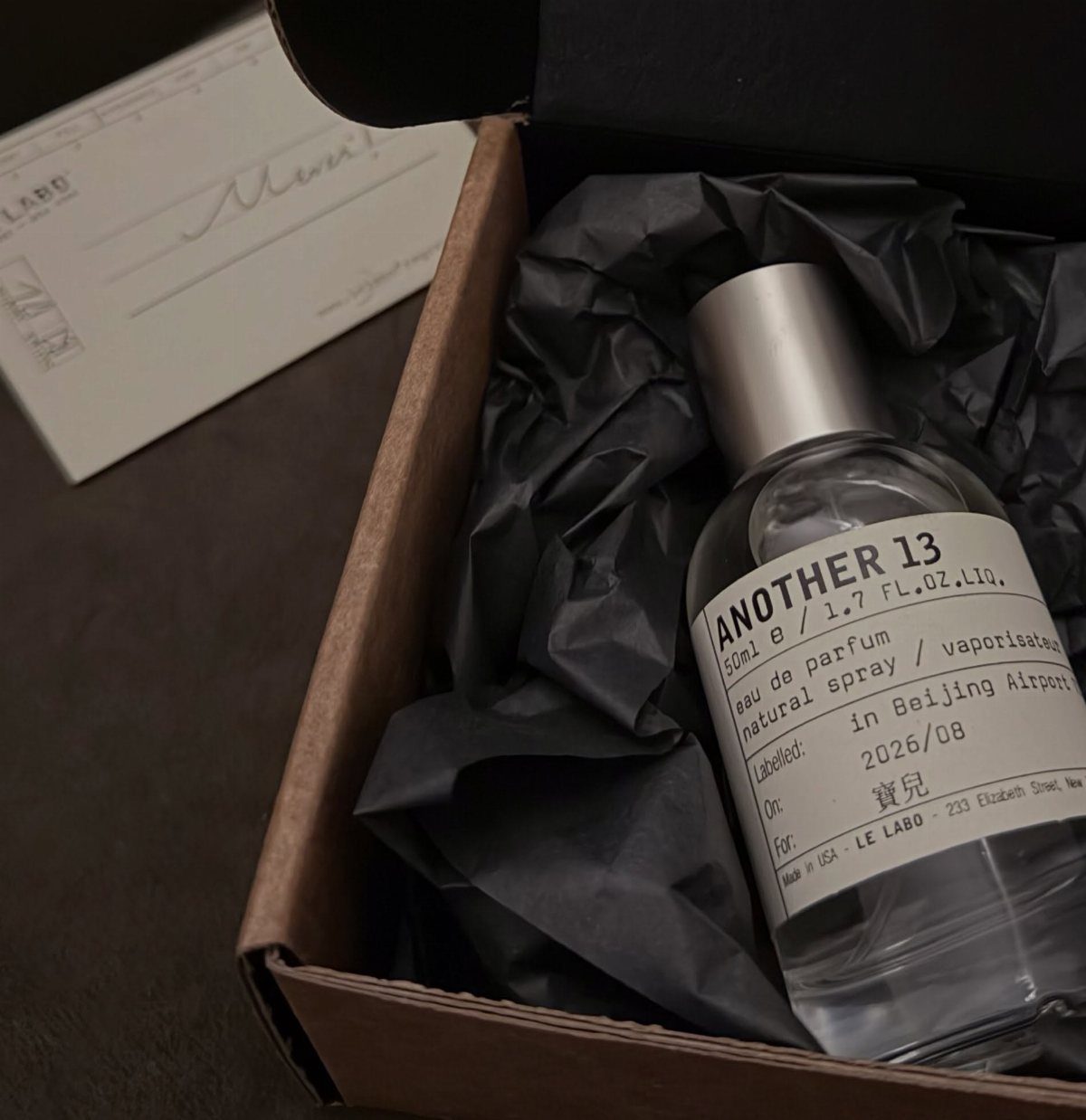 Le Labo Another 13 perfume bottle nestled in black tissue paper inside a box.