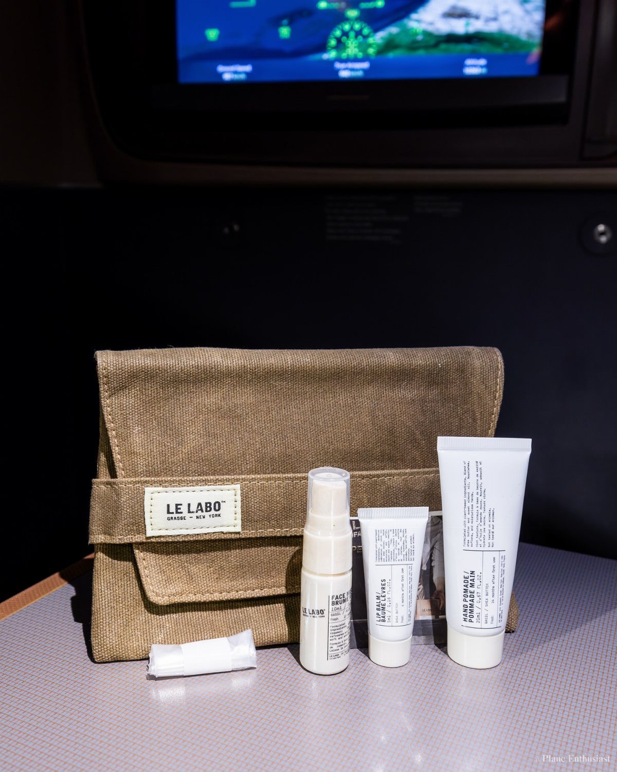 Le Labo travel beauty set with canvas pouch and white skincare bottles on airplane tray