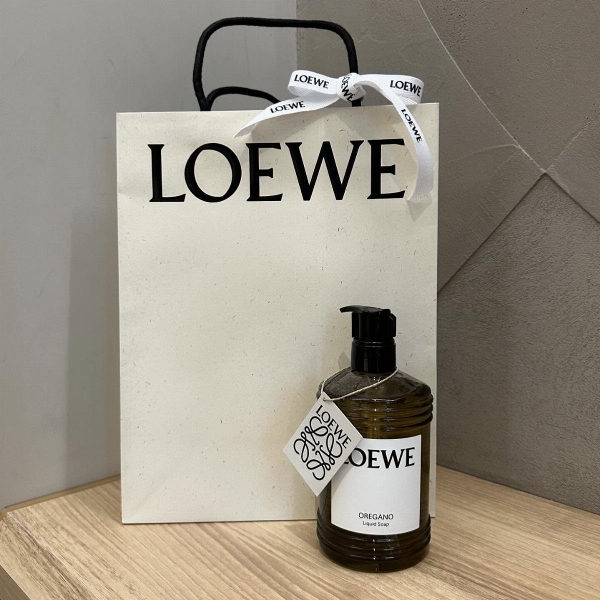 Loewe hand soap bottle and branded shopping bag on a light wooden surface.