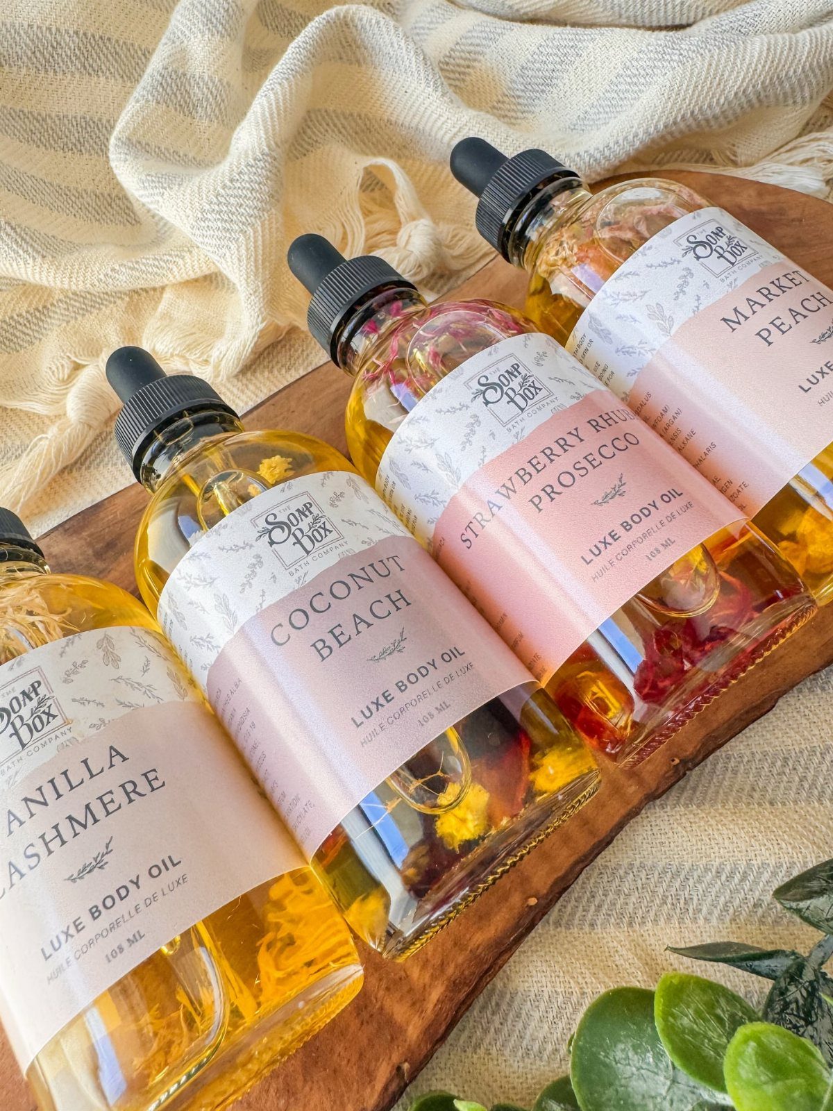Four bottles of scented luxe body oil with botanical infusions on a wooden board.