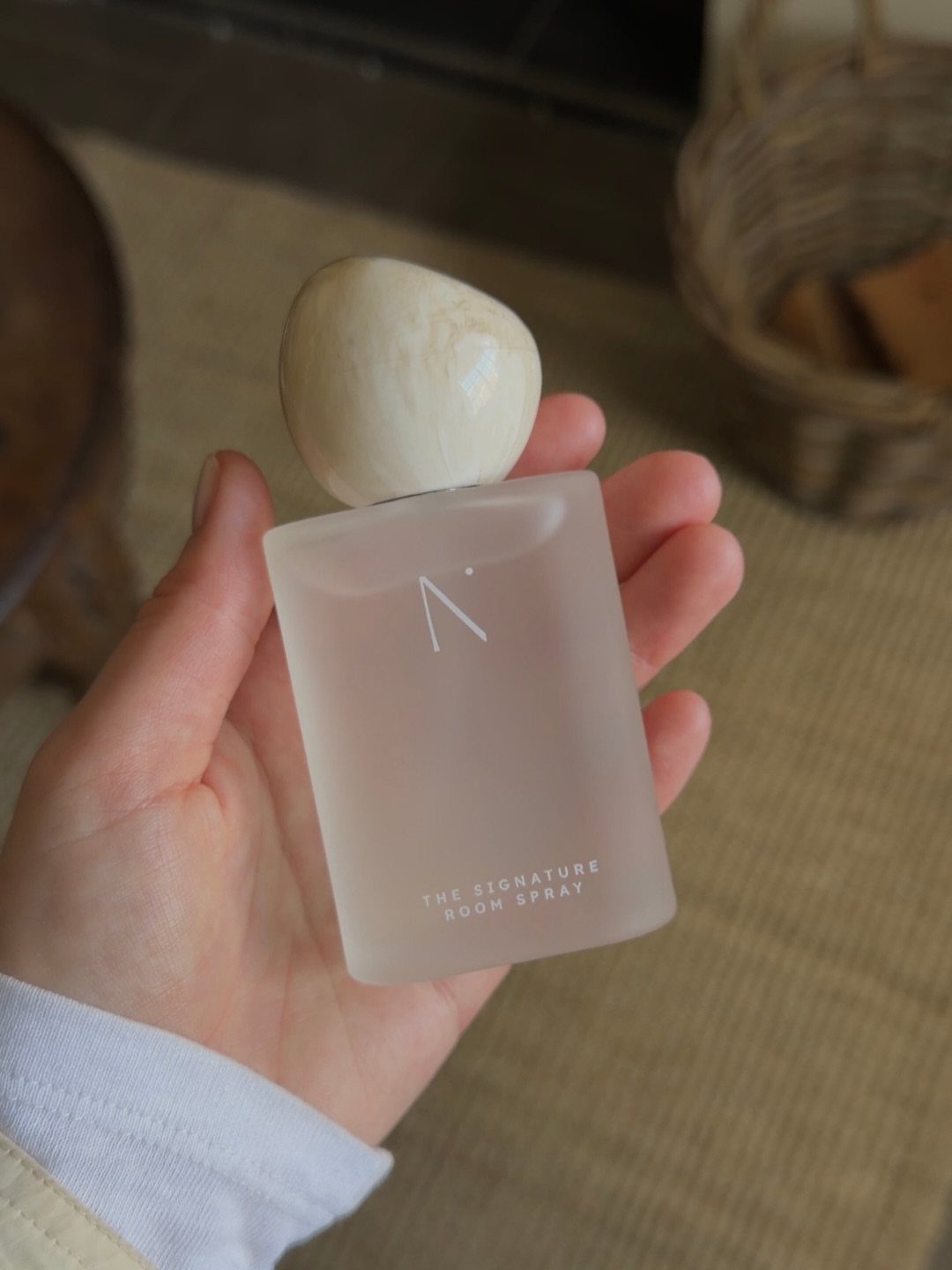 Frosted glass room spray bottle with a stone cap held in a hand