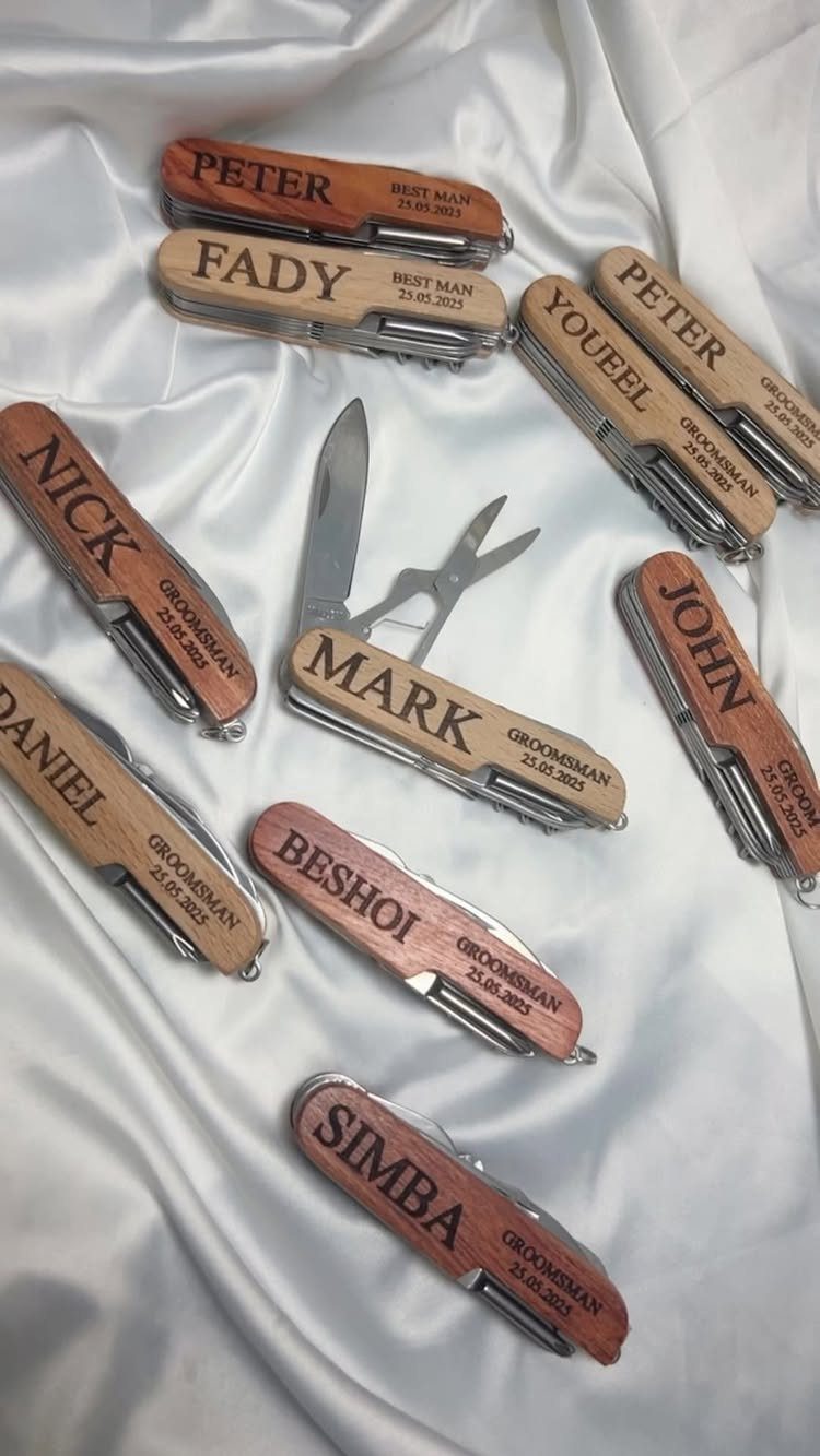 Engraved wooden pocket knives for groomsmen arranged on white satin fabric.