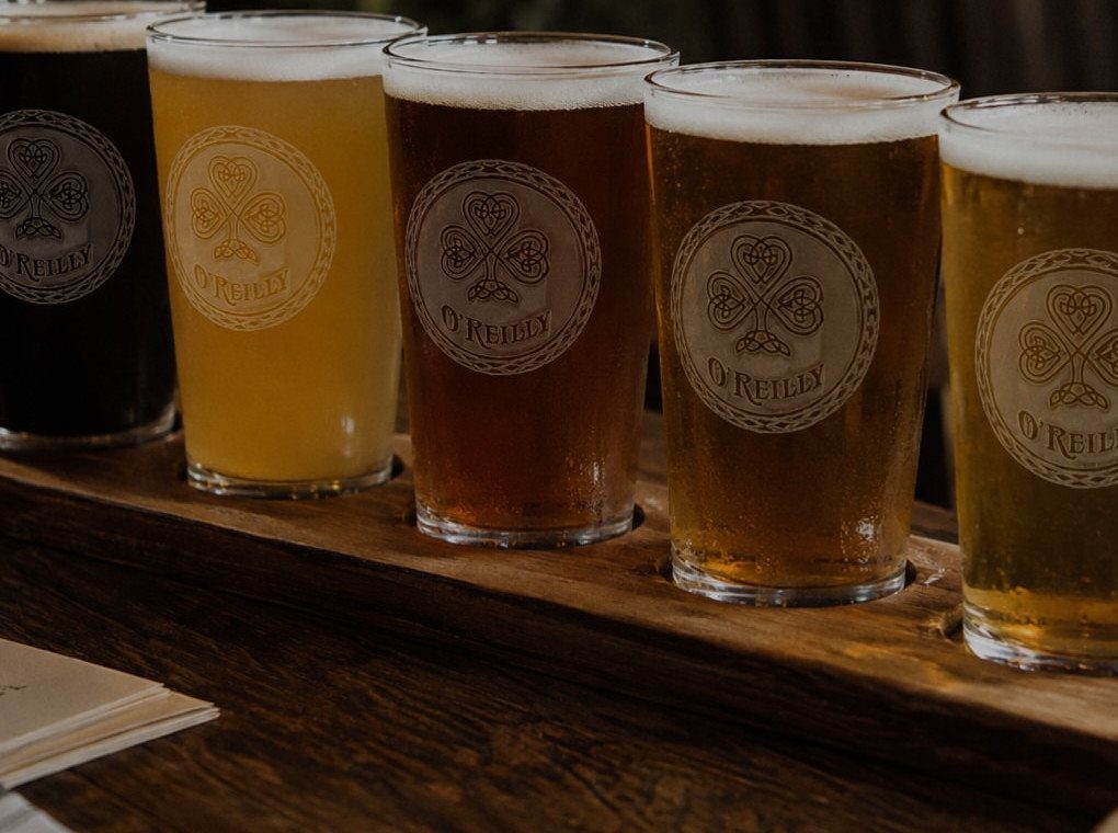 Five beer glasses with etched O'Reilly logos on a wooden flight board.