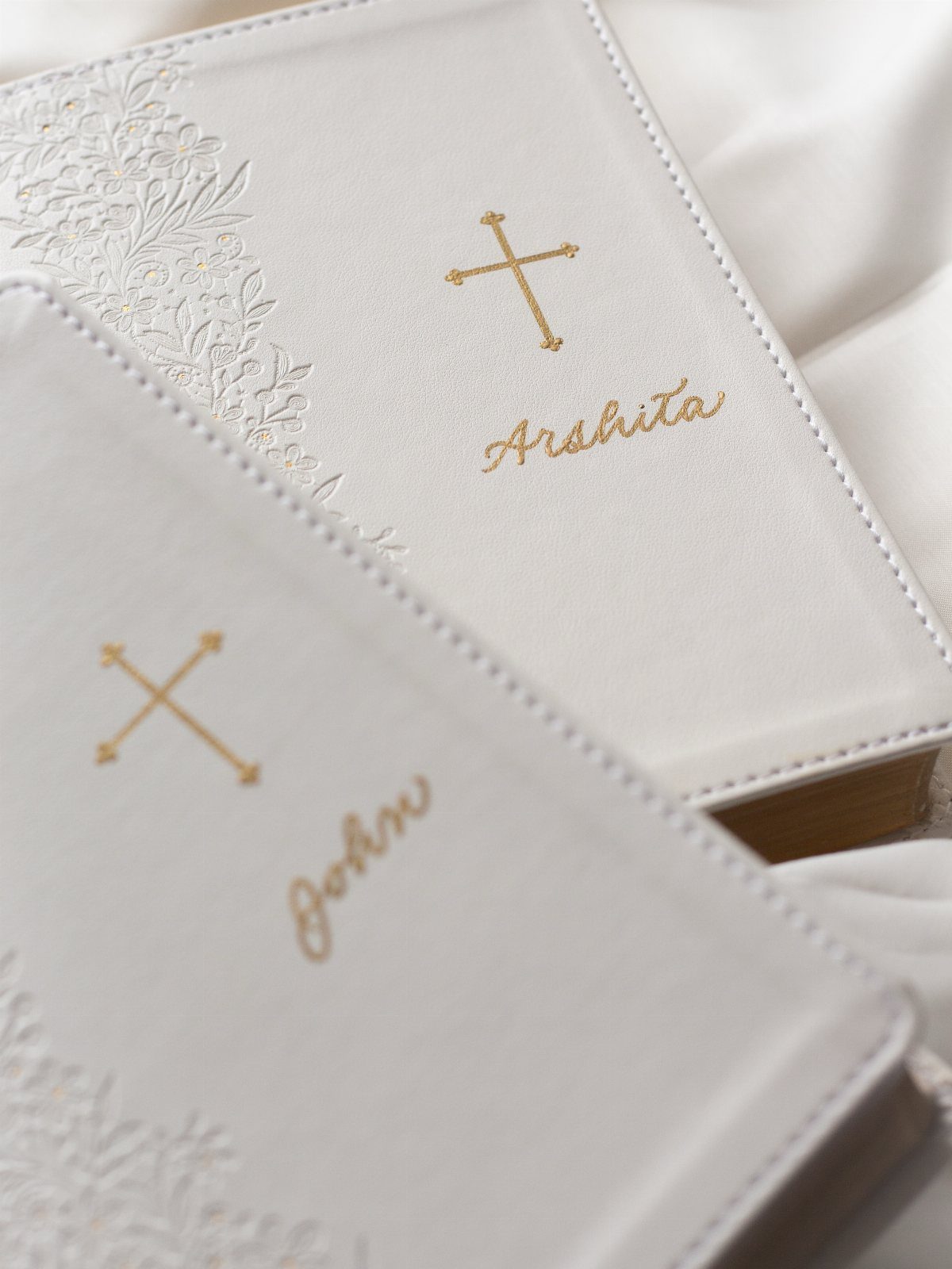 Two white leather Bibles with gold crosses and personalized names on the covers.