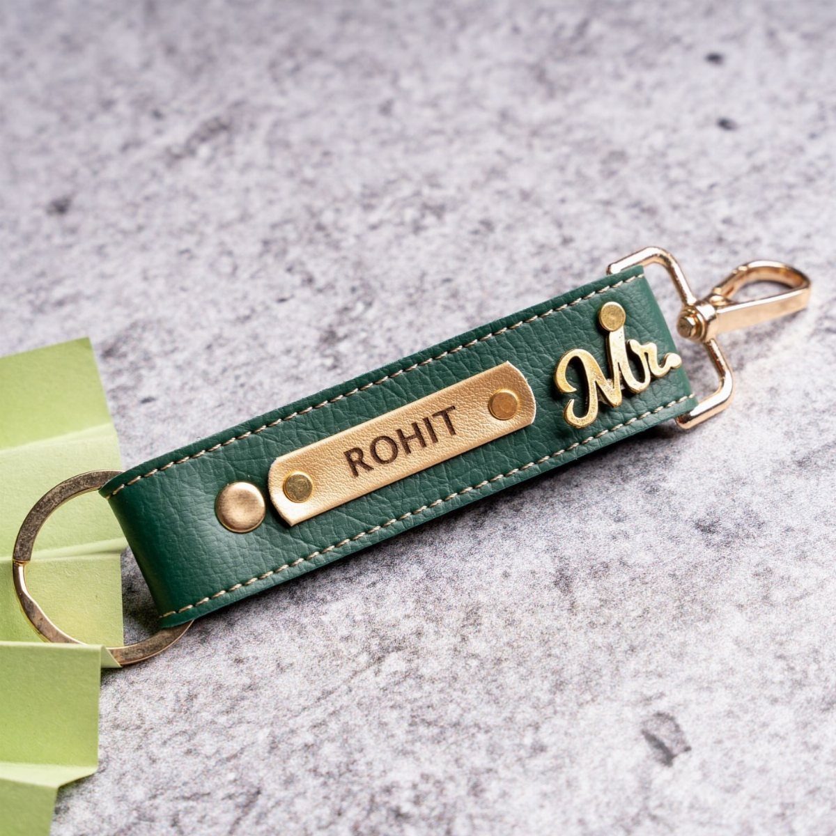 Green leather keychain with engraved name Rohit and gold Mr. charm on stone.