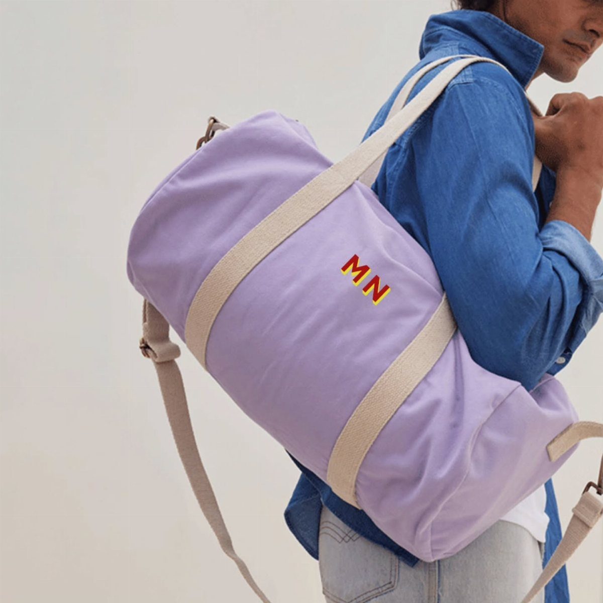 Light purple canvas duffle bag with red embroidered initials carried by a man.