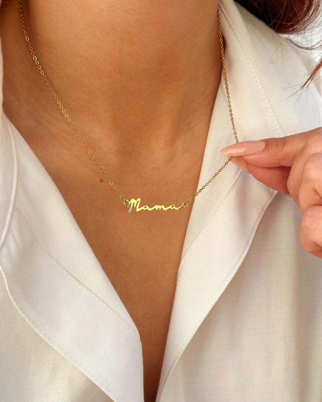 Gold script necklace reading Mama worn by a person in a white shirt