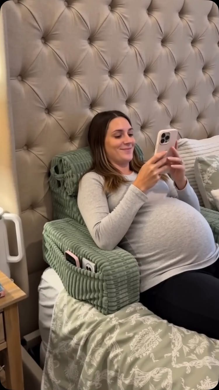Pregnant woman leaning against a sage green corduroy pregnancy pillow in bed.
