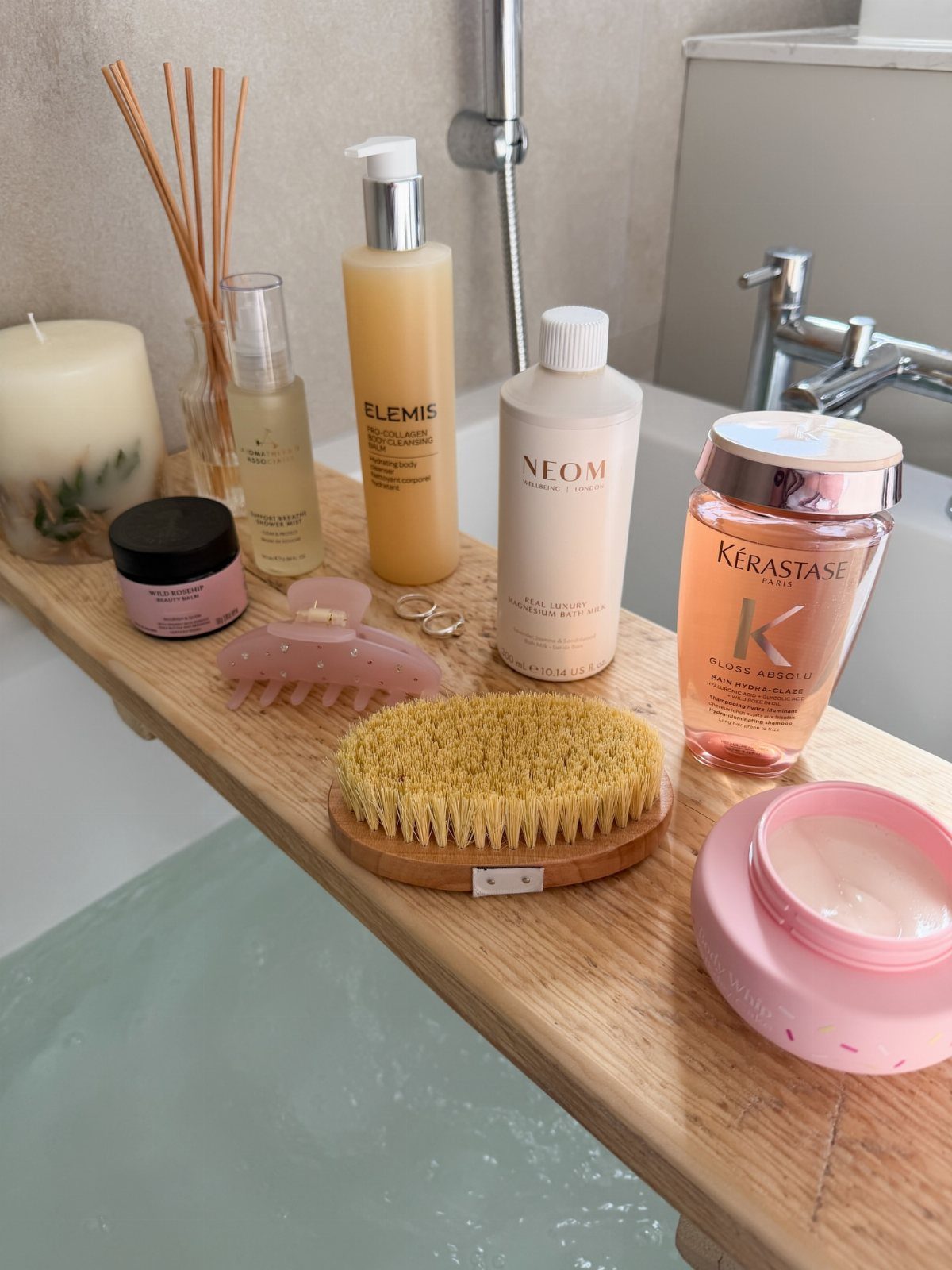 Skincare products and a body brush arranged on a wooden bathtub caddy.
