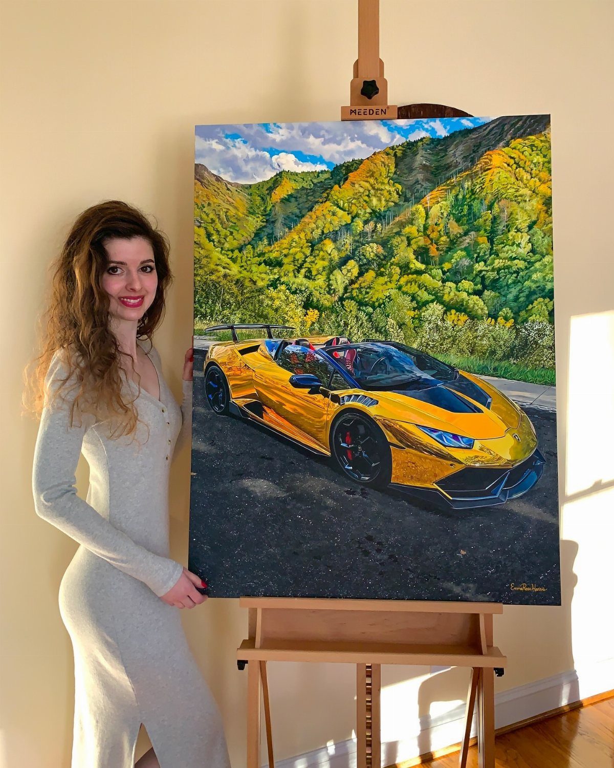 12 Paintings as Gifts for Every Budget and Taste 6 Woman standing beside a painting of a yellow sports car on a wooden easel