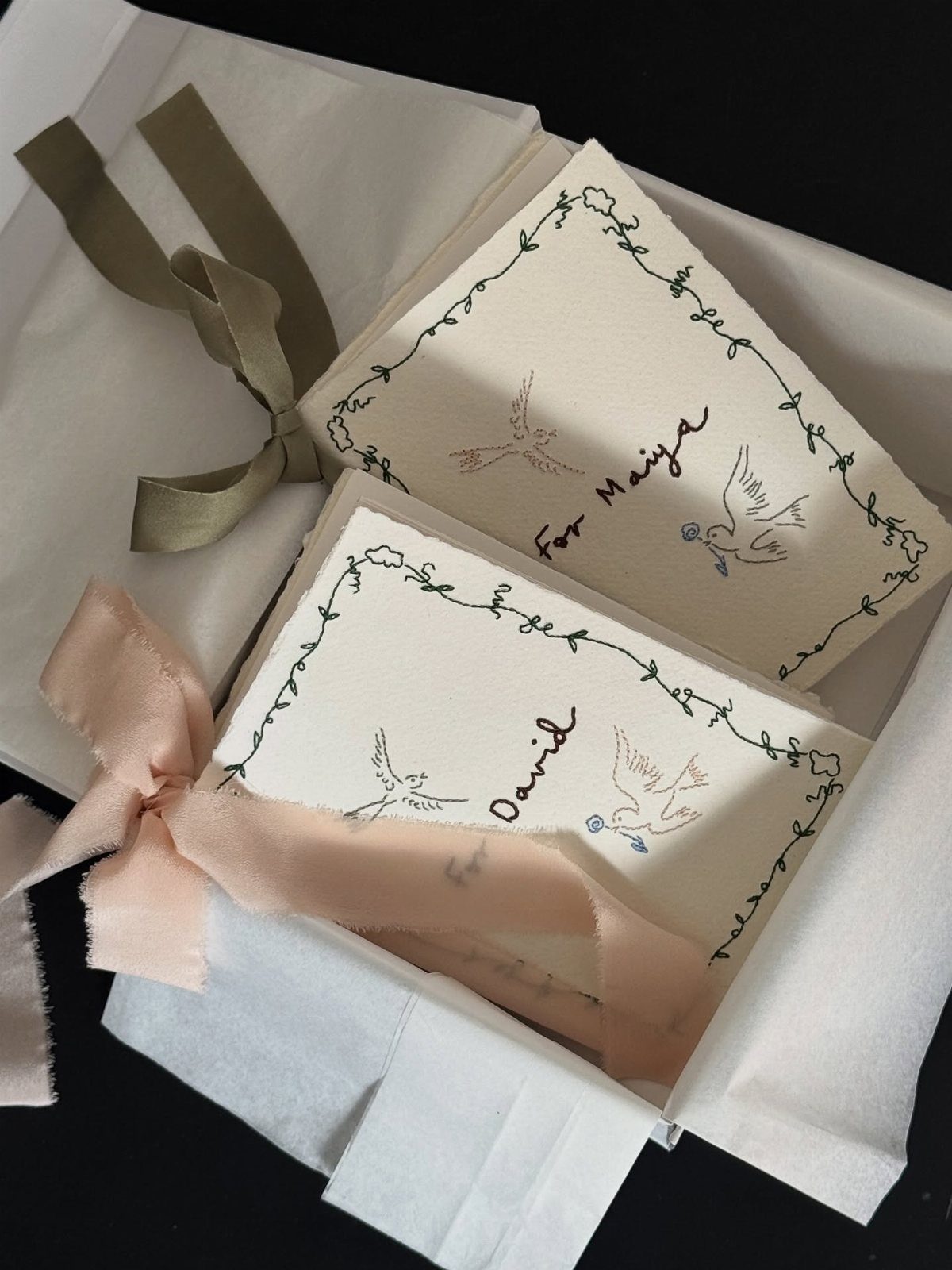 Two personalized wedding vow booklets with bird illustrations and ribbons in a box.