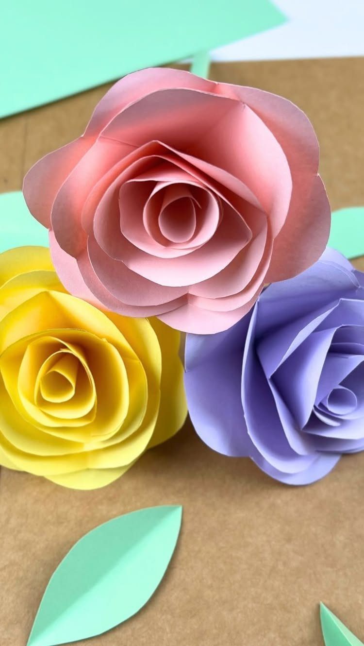 Three colorful paper roses in pink, yellow, and purple with green paper leaves.