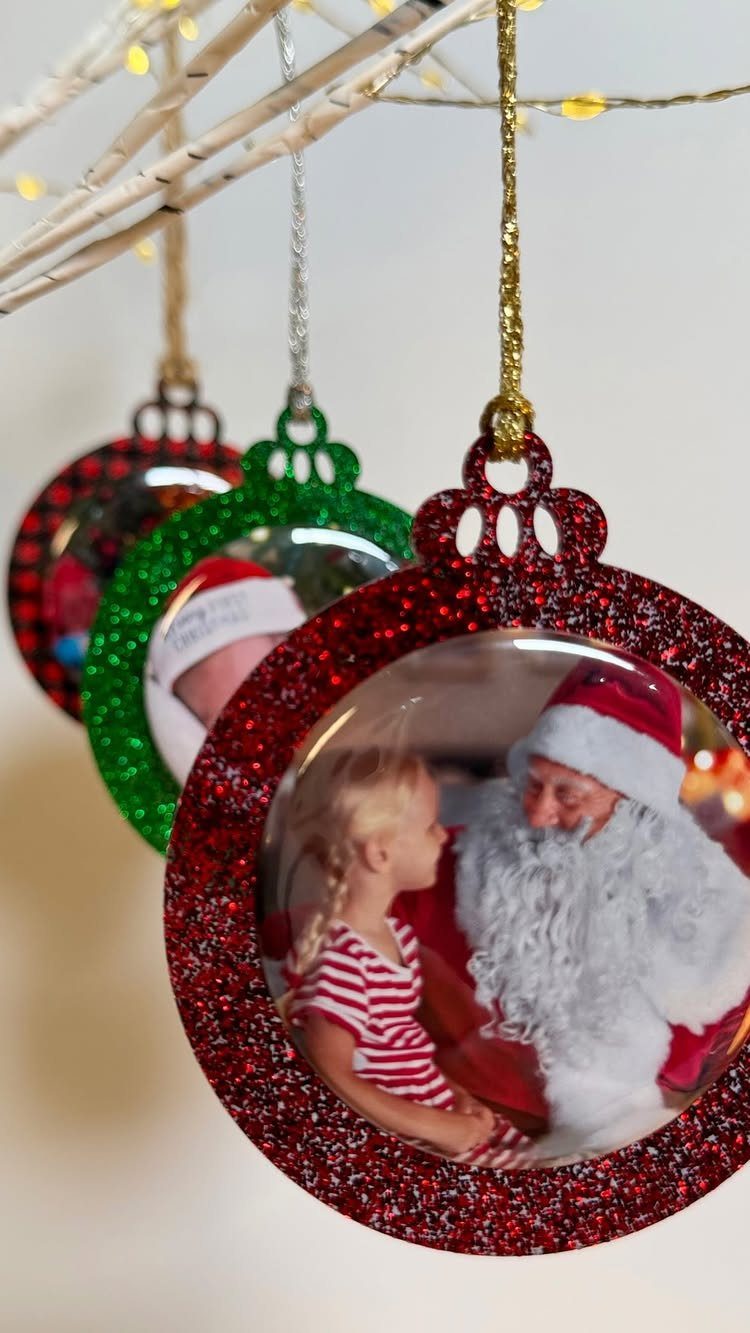 Circular Christmas ornaments with glittery frames containing personalized photos hanging from birch branches.