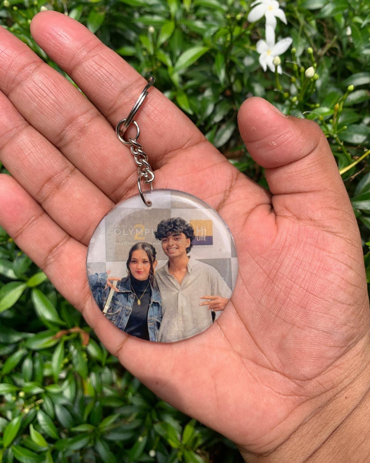 Circular photo keychain featuring a couple, held in a hand against green leaves.