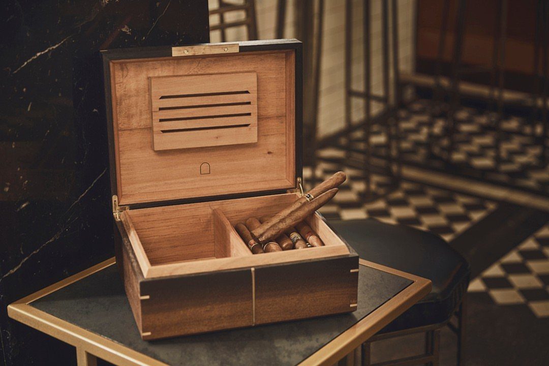 Wooden cigar humidor open on a table containing several brown cigars.