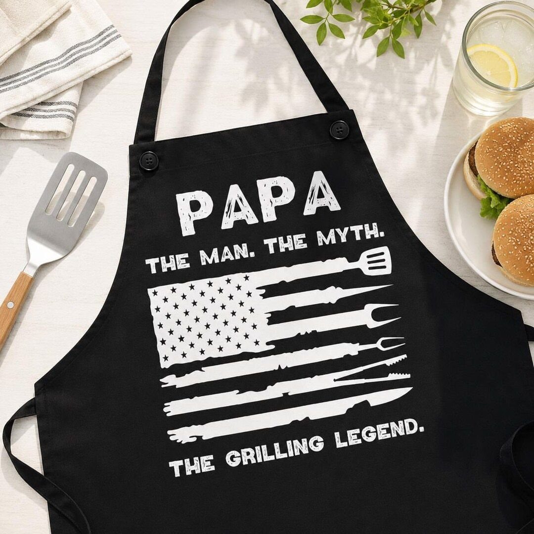 Black apron with grilling legend text and tool flag next to burgers