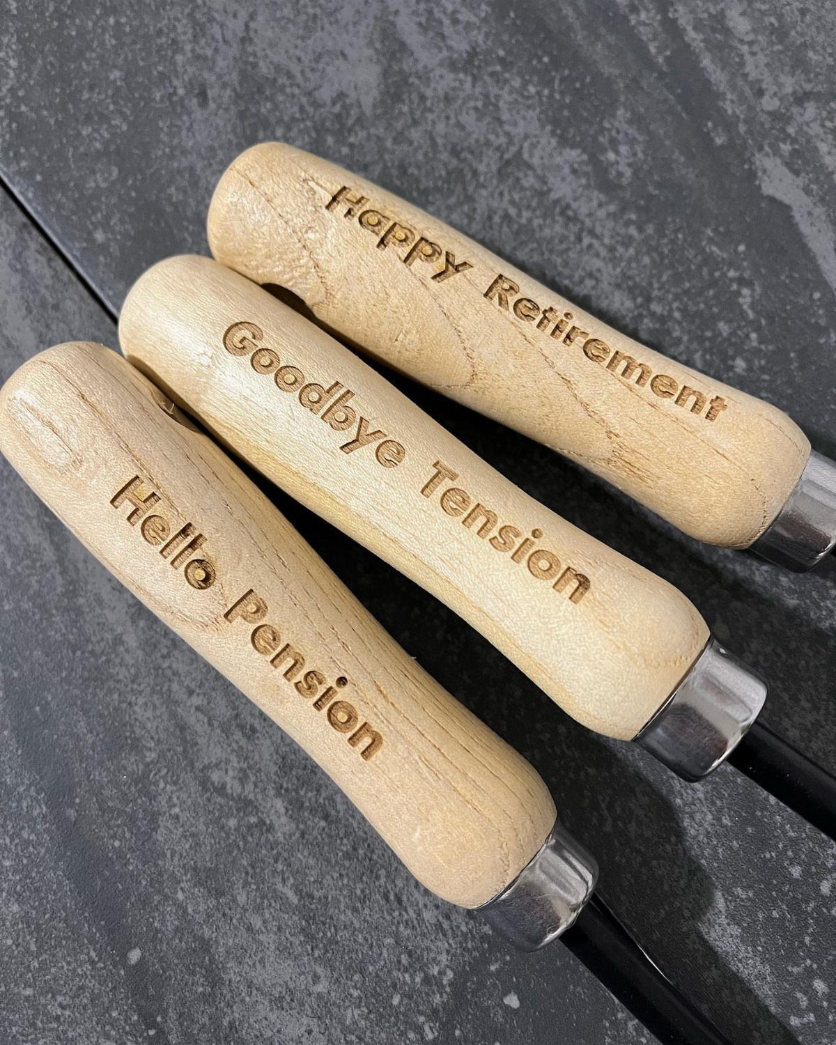 Engraved wooden handles of gardening tools with retirement messages on a dark surface