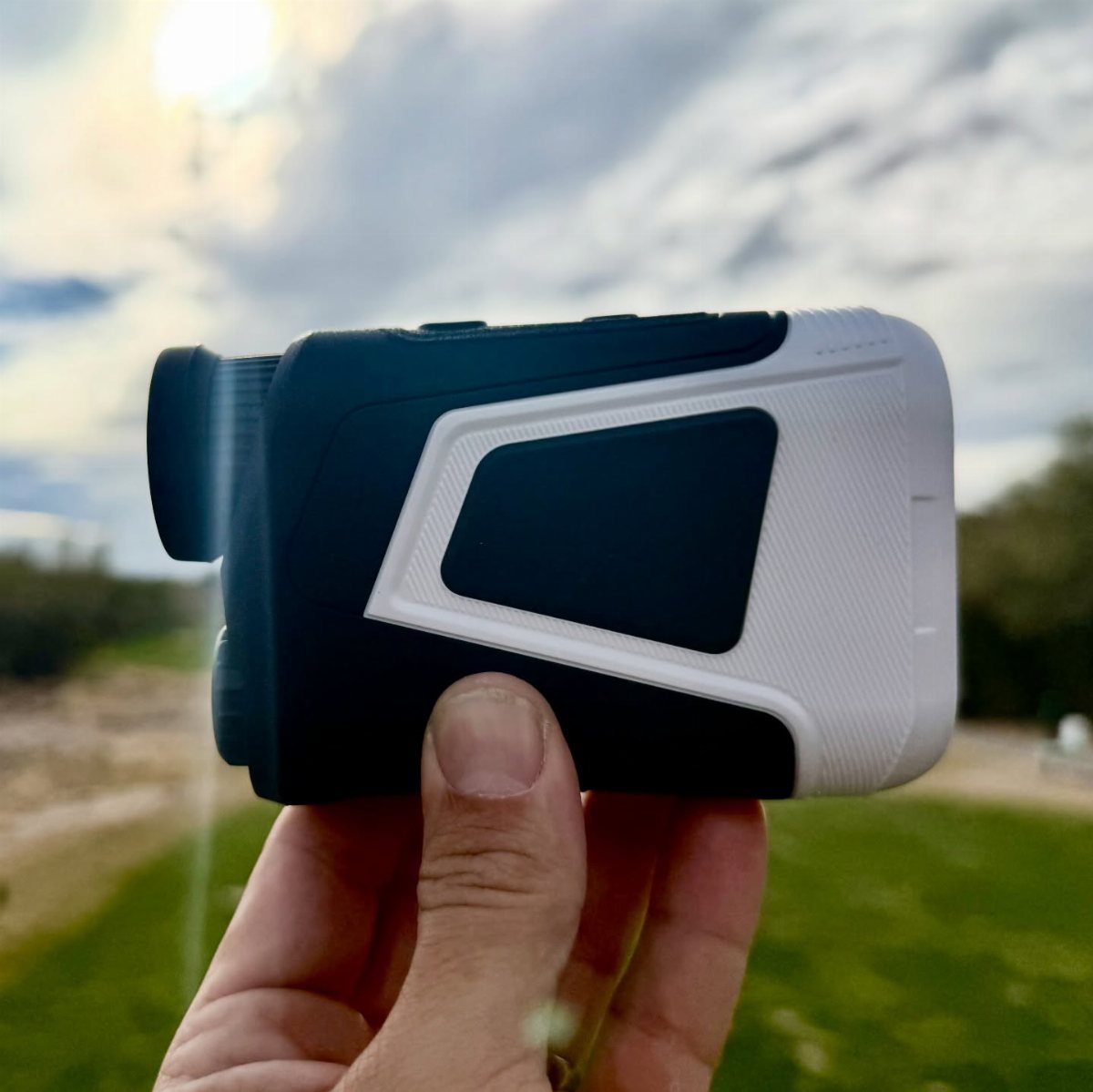 Golf rangefinder held in a hand over a green golf course background.
