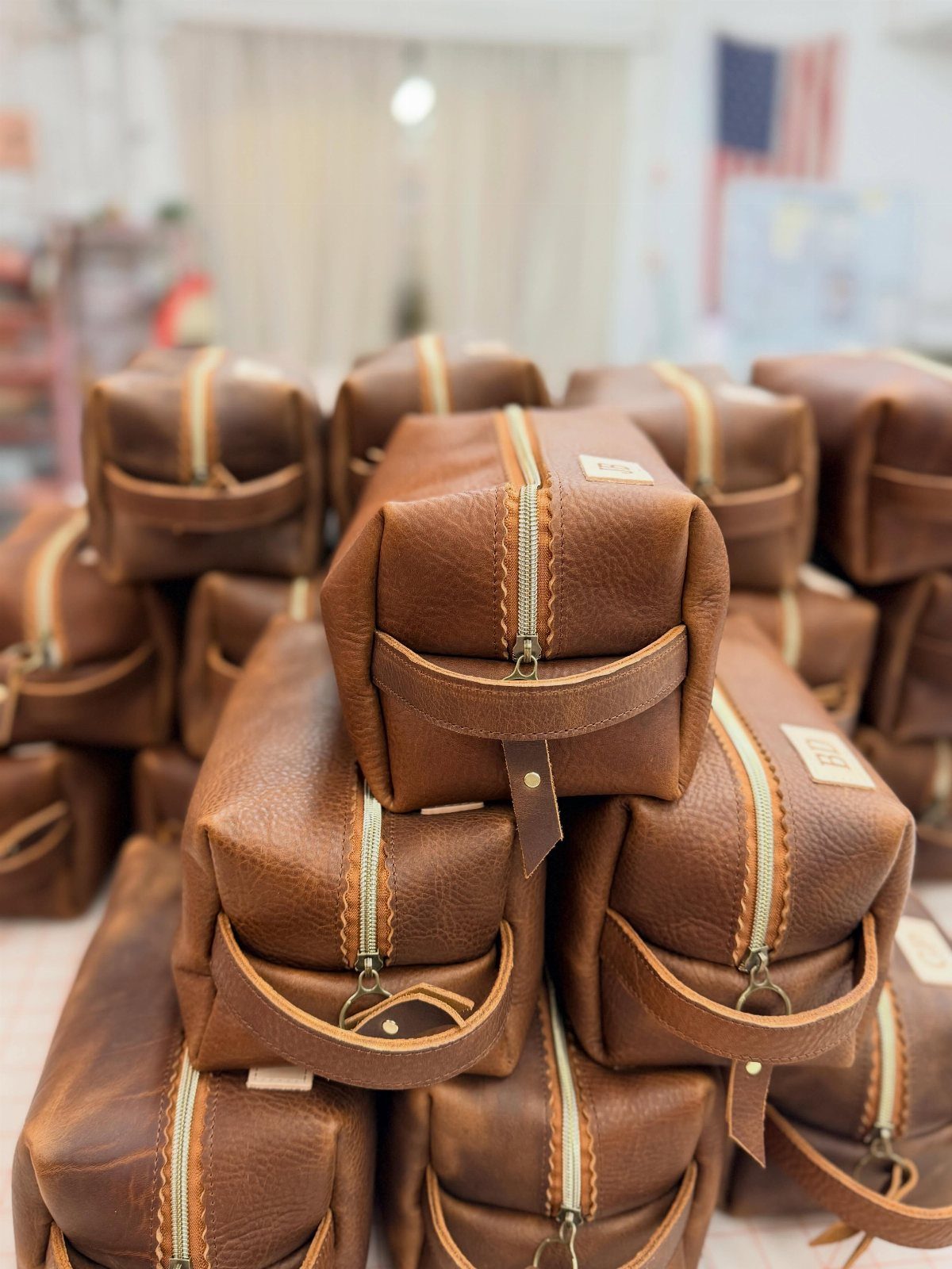 Brown leather dopp kits stacked together, featuring zippers and sturdy handles.