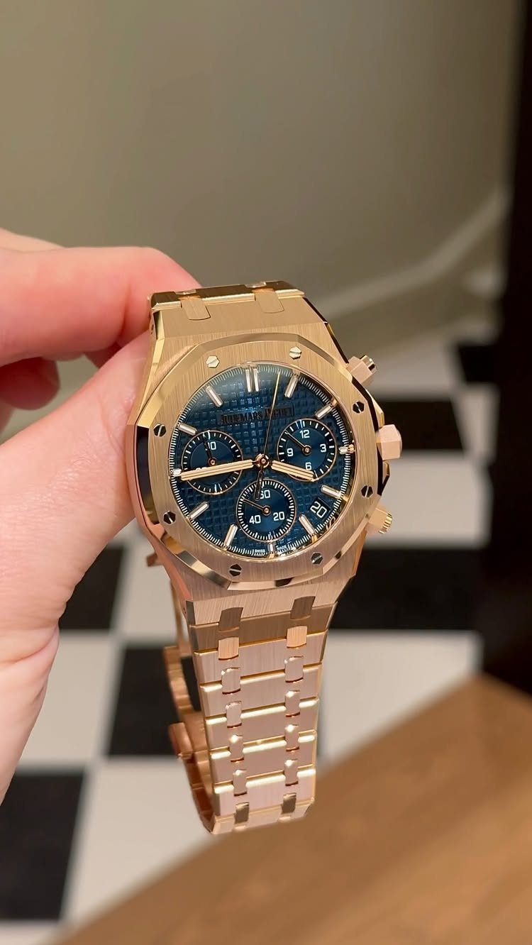 Gold luxury wristwatch with a blue dial held by a person's hand.