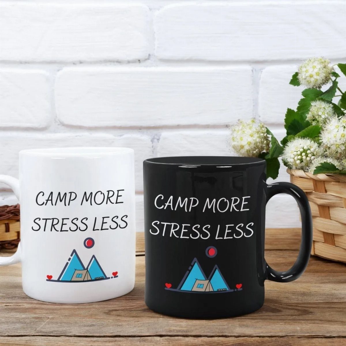 Two ceramic mugs with camping graphics and text on a wooden table.