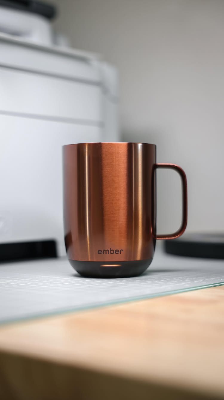 Copper metallic Ember smart mug sitting on a desk in a bright room.