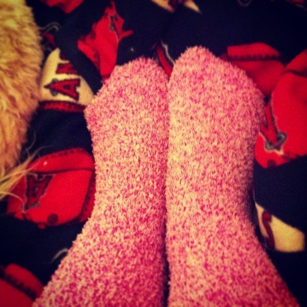 Fuzzy pink and purple socks on feet resting on patterned fabric.