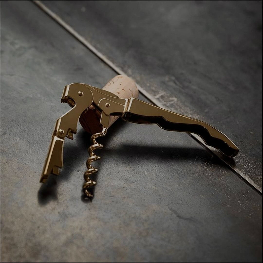 Gold metal corkscrew resting on a dark grey textured surface with a cork.