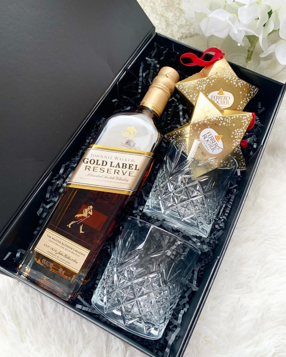 Whisky bottle and crystal glasses in a black gift box with gold stars.