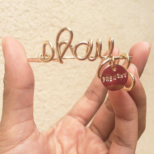 Gold wire bracelet spelling okay with a red charm held in a hand