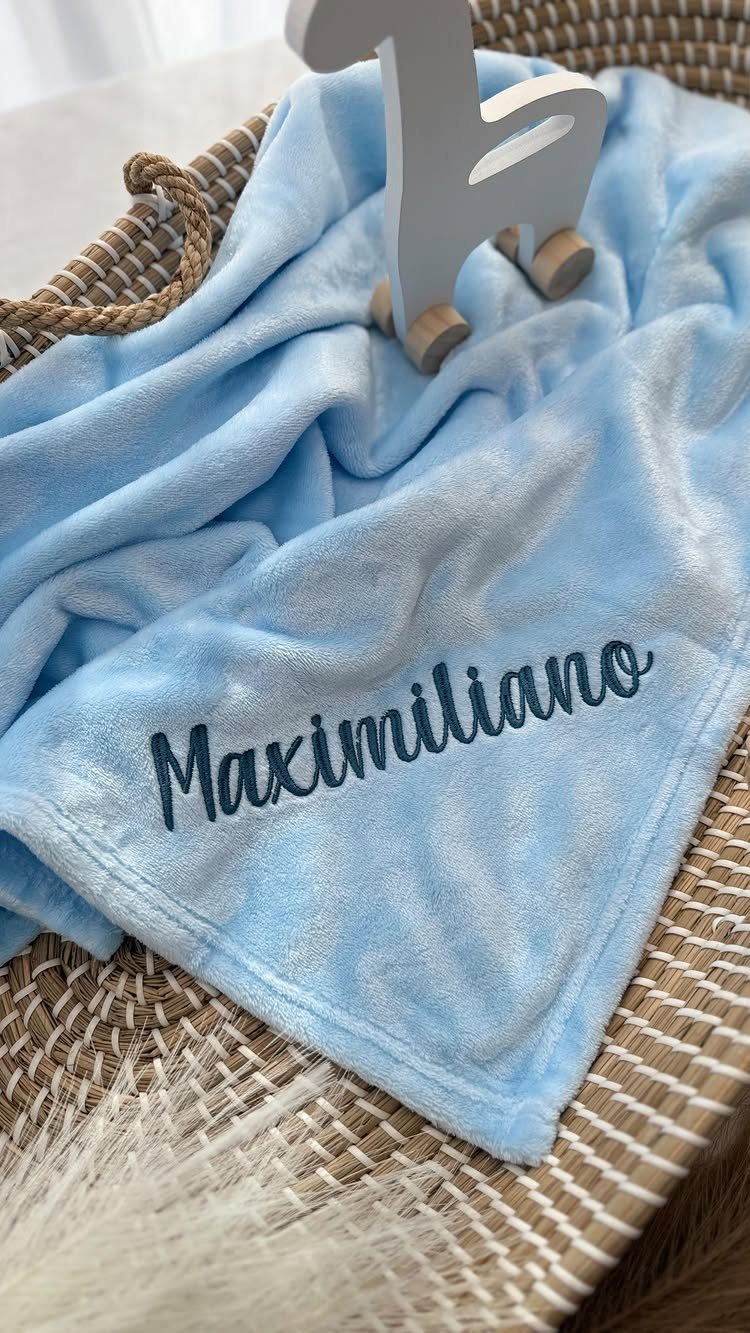 Light blue personalized baby blanket with embroidered name in a wicker basket