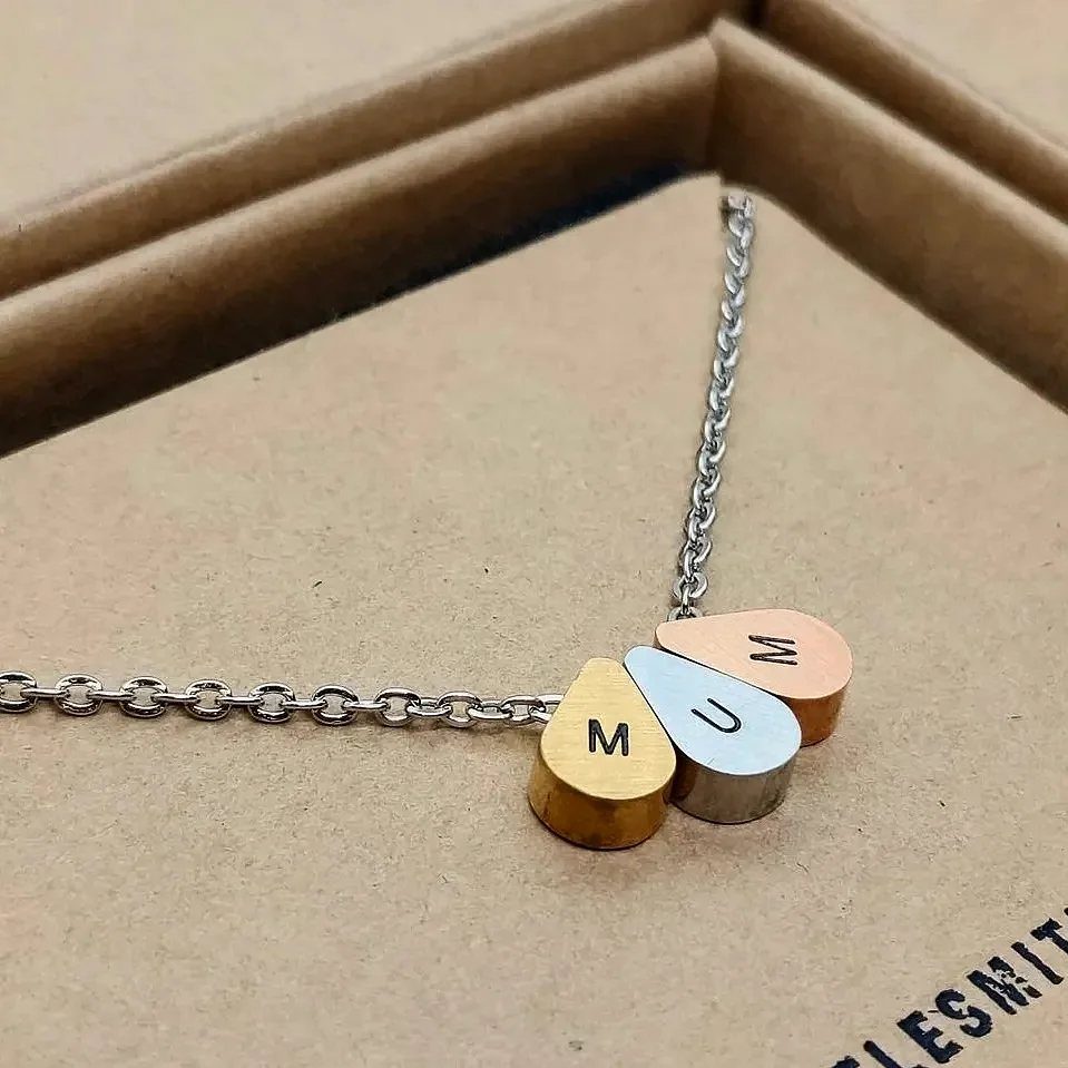 Silver chain necklace with three engraved metal teardrop charms on brown cardboard.
