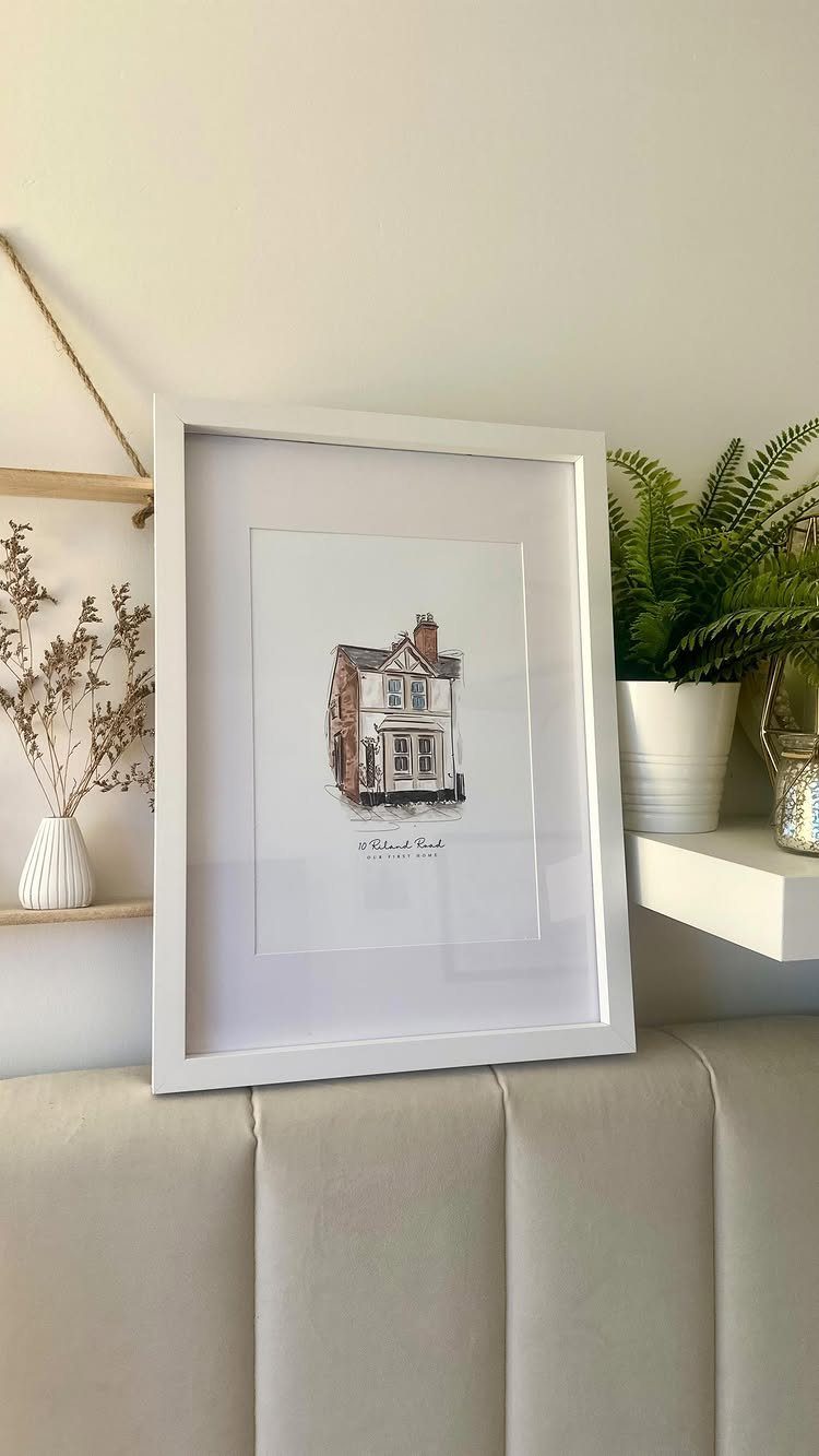 Framed custom painting of a house resting on a beige upholstered headboard.