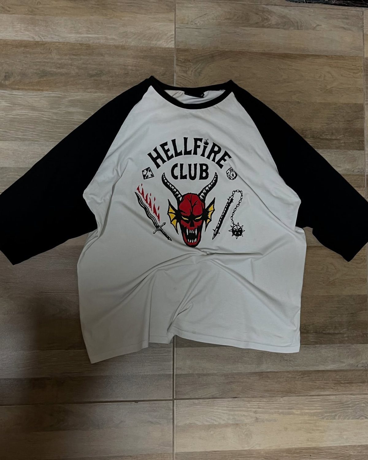 Hellfire Club baseball shirt with red devil graphic on a wooden floor
