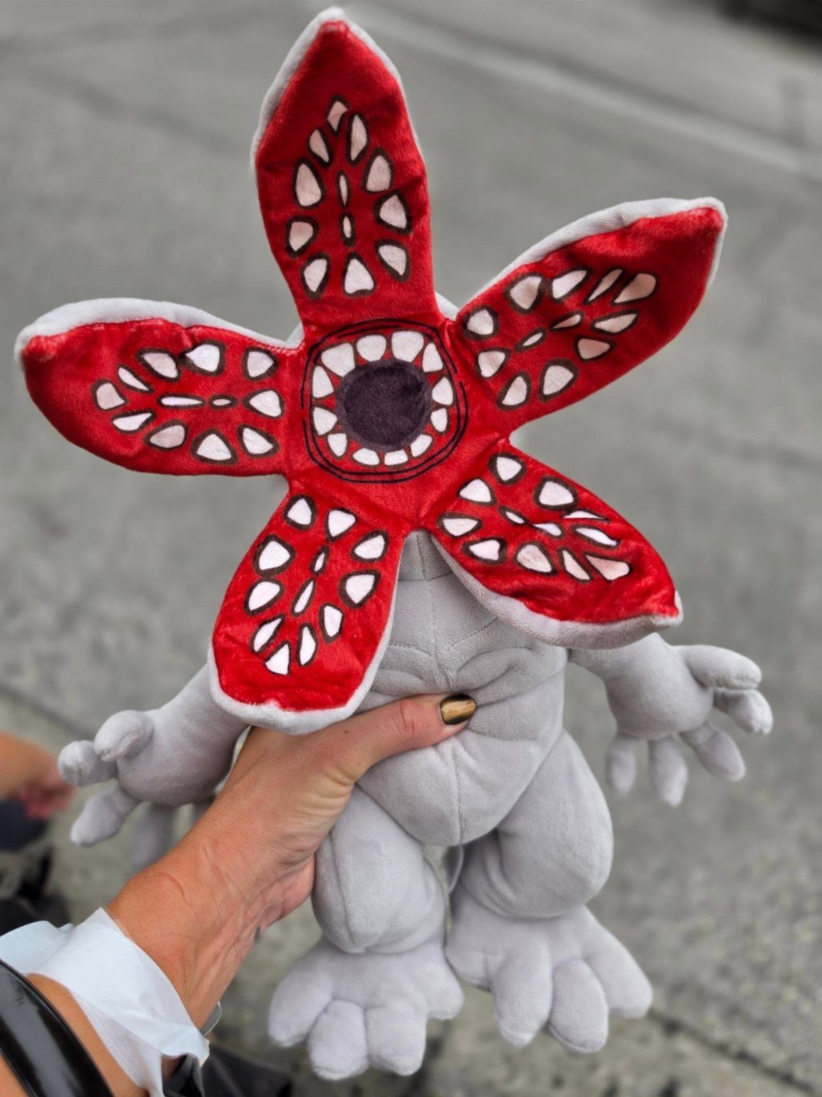 Grey Demogorgon plush toy with a red open mouth held by a hand.