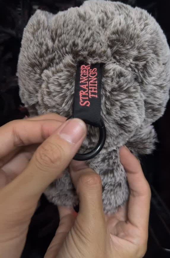 Grey faux-fur keychain with a red Stranger Things logo tag held by hands.