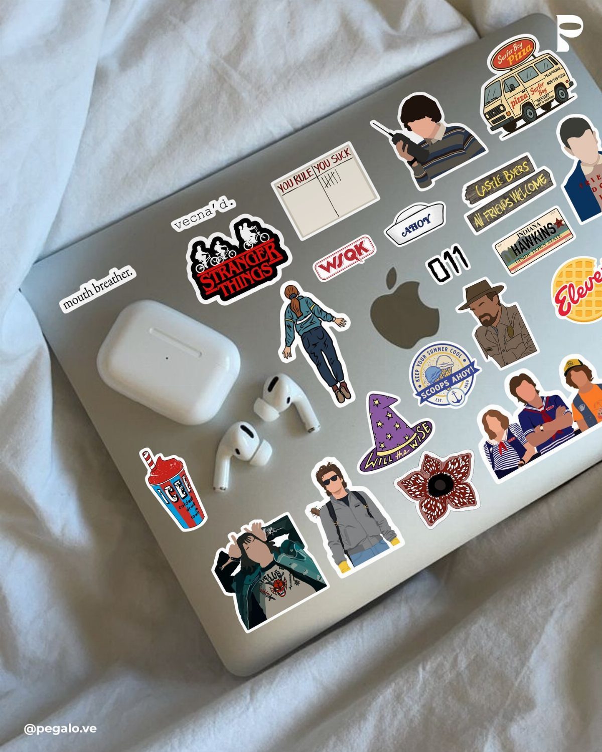 Stranger Things vinyl stickers decorating a silver laptop lid with wireless earbuds.