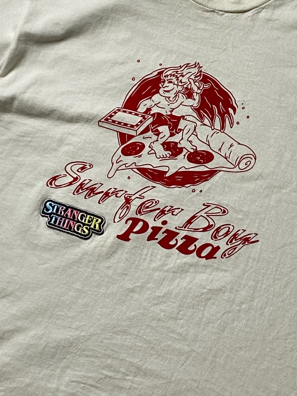 White t-shirt with Surfer Boy Pizza graphic and Stranger Things logo patch
