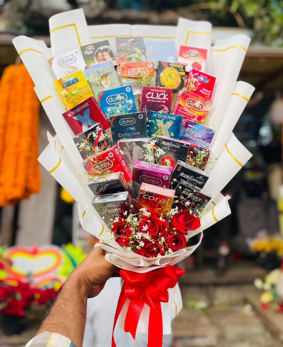 Bouquet of red roses and various condom brands wrapped in white paper.