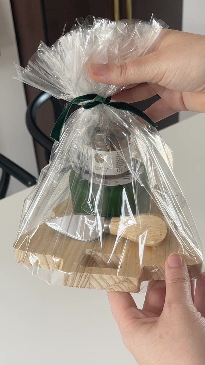 Gift set with wooden board, cheese knife, and jar wrapped in cellophane.