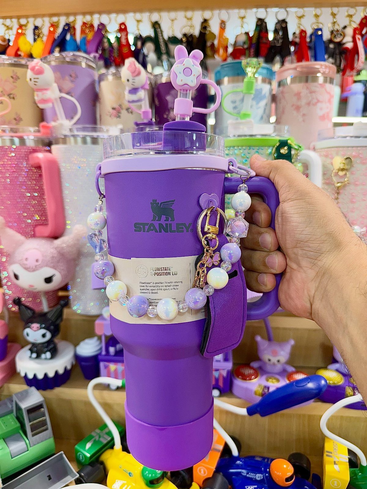 Purple Stanley tumbler with beaded charms held by a hand in a store.