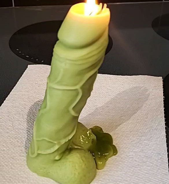 Light-green penis-shaped candle lit and resting on a white paper napkin.