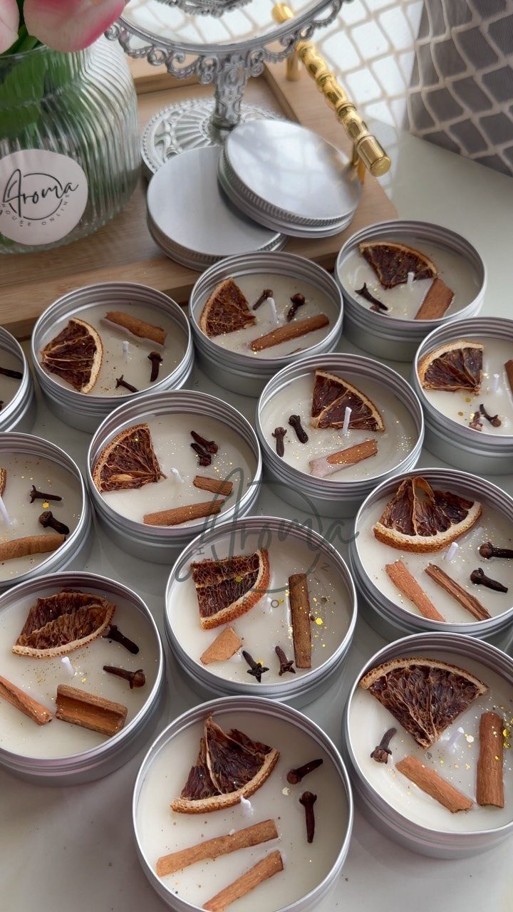 White wax candles in silver tins decorated with dried orange and cinnamon sticks.