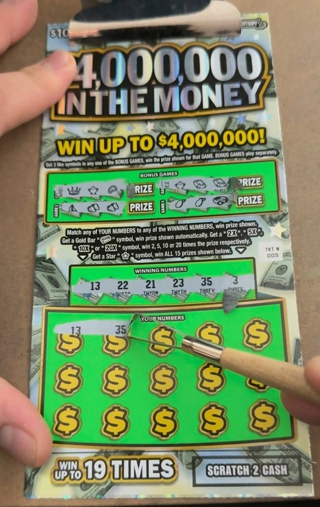 Scratch-off lottery ticket being revealed with a small paintbrush held by hands.