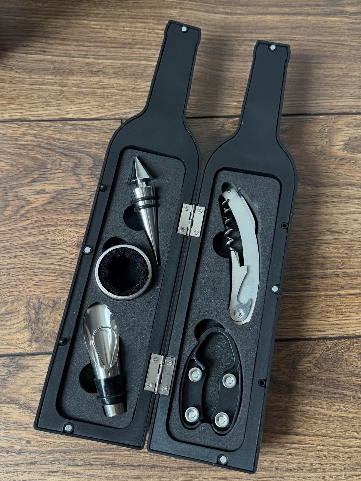 Black wine accessory kit case with silver tools on a wooden table.
