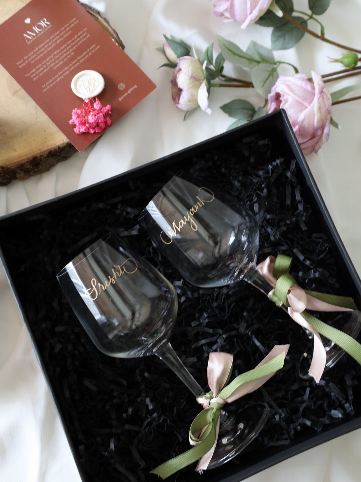 Two engraved wine glasses with gold names in a black gift box with ribbons.