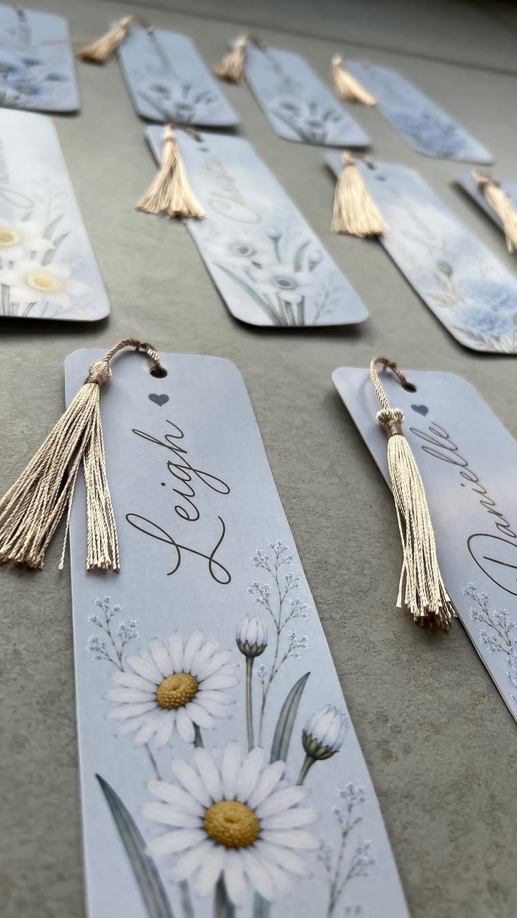 Personalized light blue bookmarks with daisy flowers and gold tassels on grey background