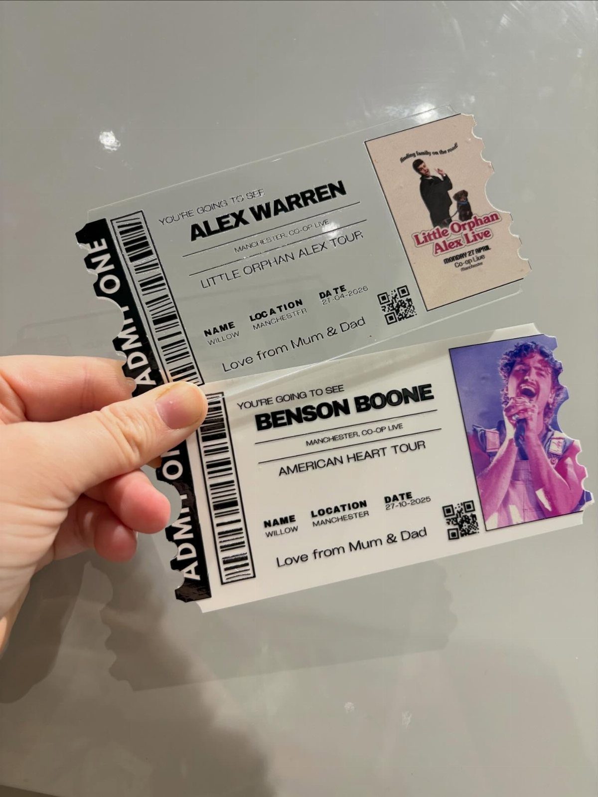 Hand holding two printed concert tickets for Alex Warren and Benson Boone events.