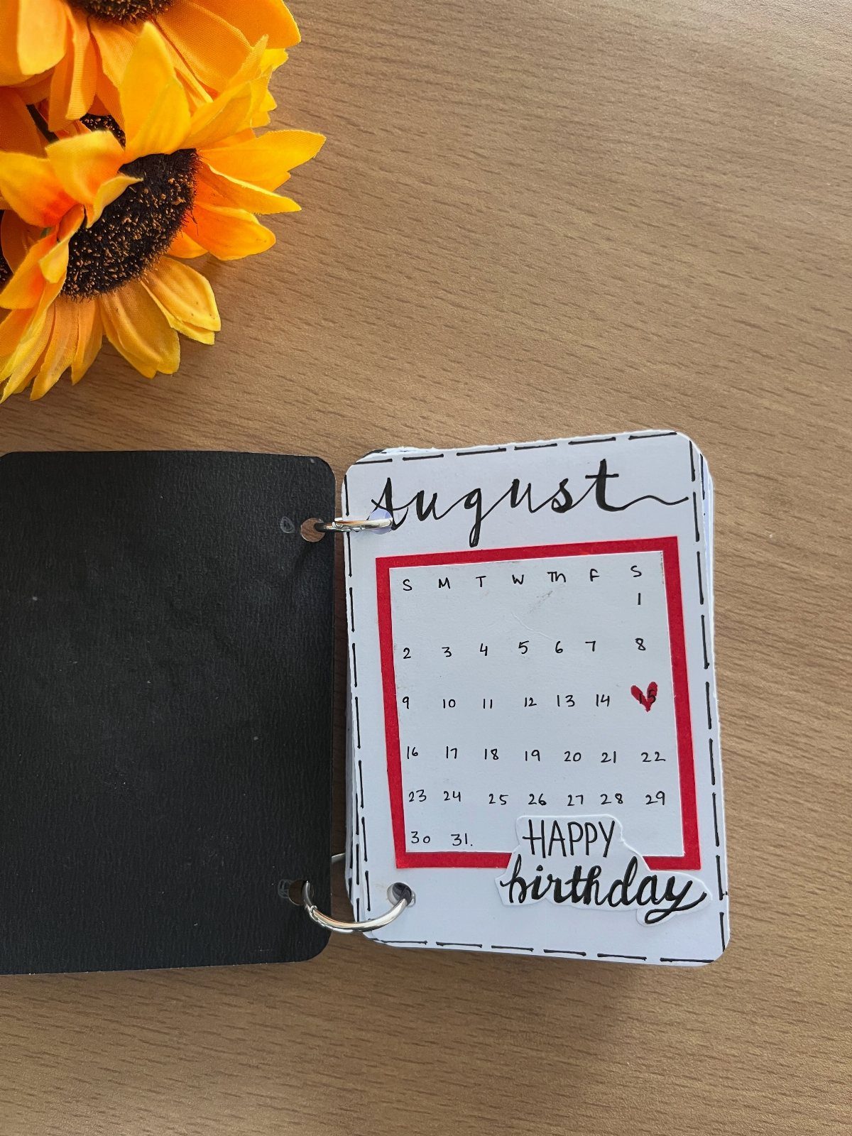 Handmade birthday calendar binder with a red heart and yellow sunflowers nearby.